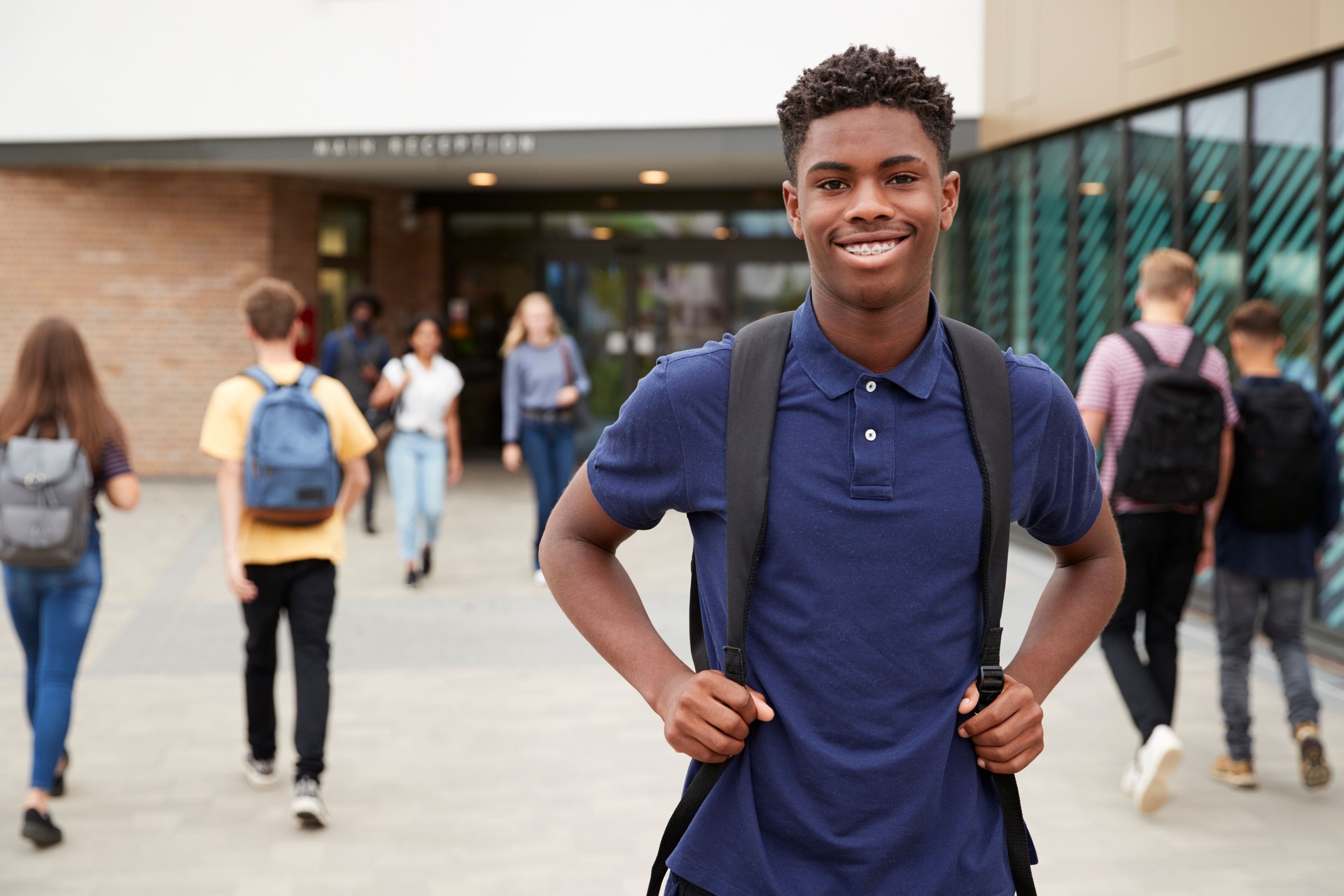 Portrait Of Smiling Male High School Student Outside College Building With Other Teenage Students In Background